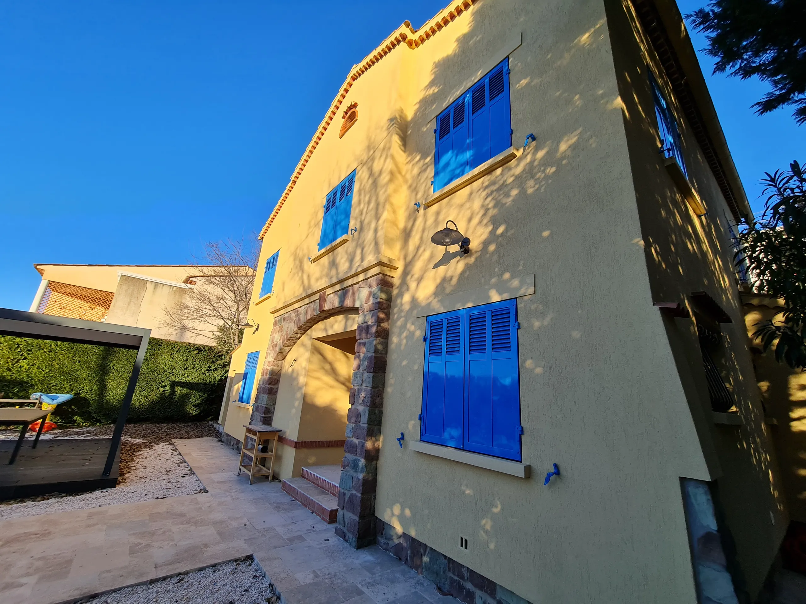 Vue d'une maison rénovée avec des fenêtres bleues et un jardin bien entretenu, mettant en avant la rénovation extérieure