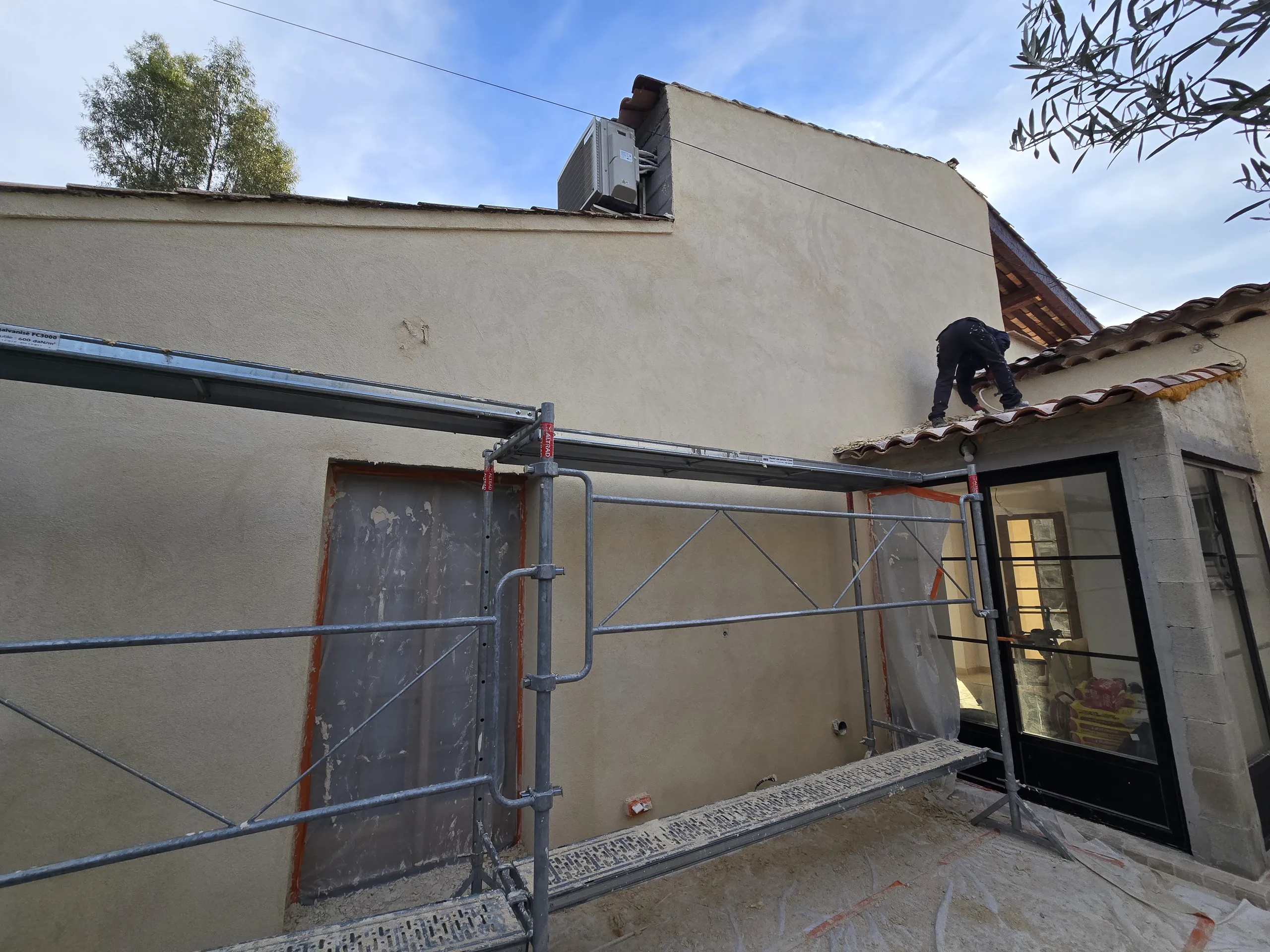 Ravalement de façade avec échafaudage, un professionnel travaille sur le toit