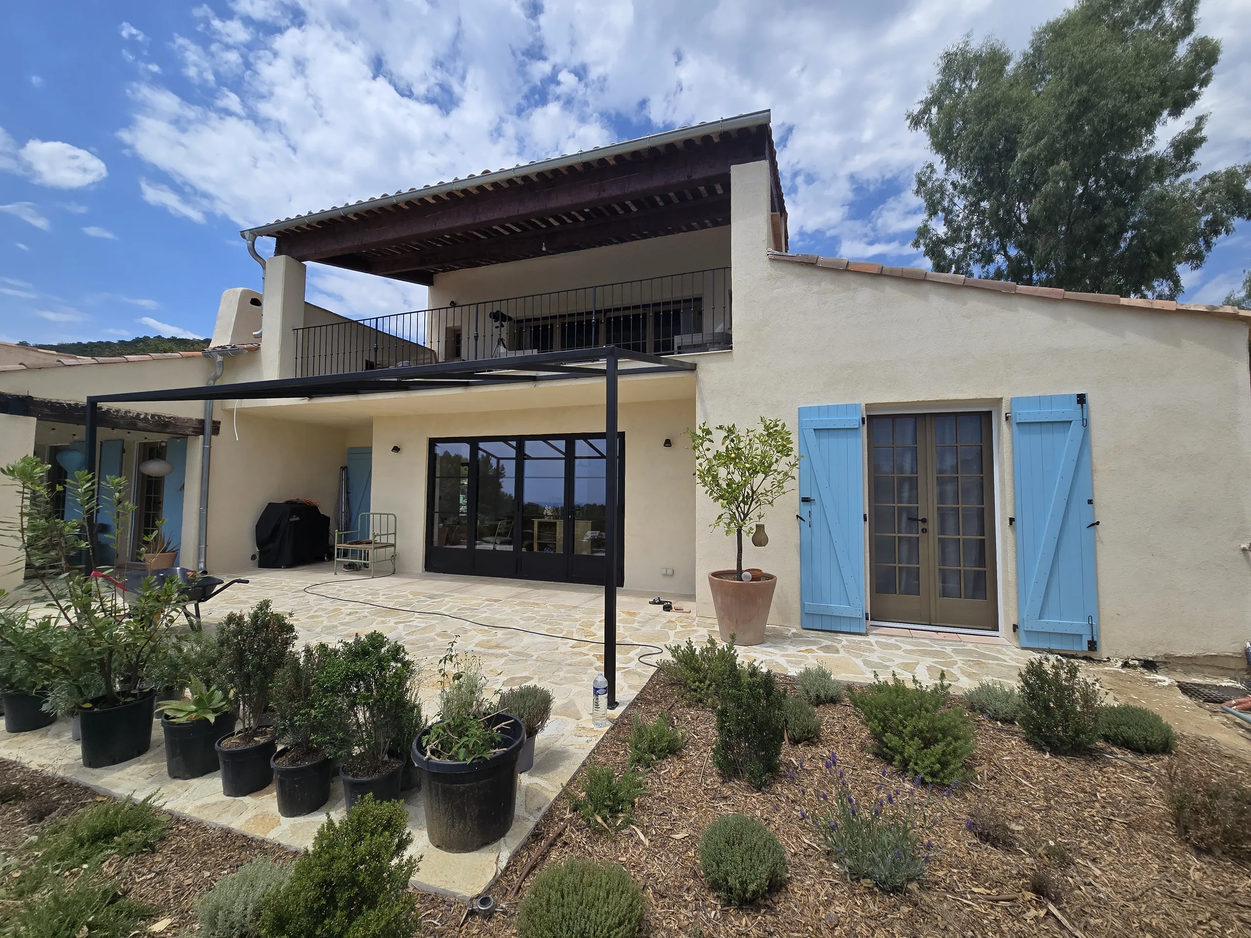 Terrasse rénovée avec des plantes et des volets bleus, mettant en avant les travaux de rénovation extérieure